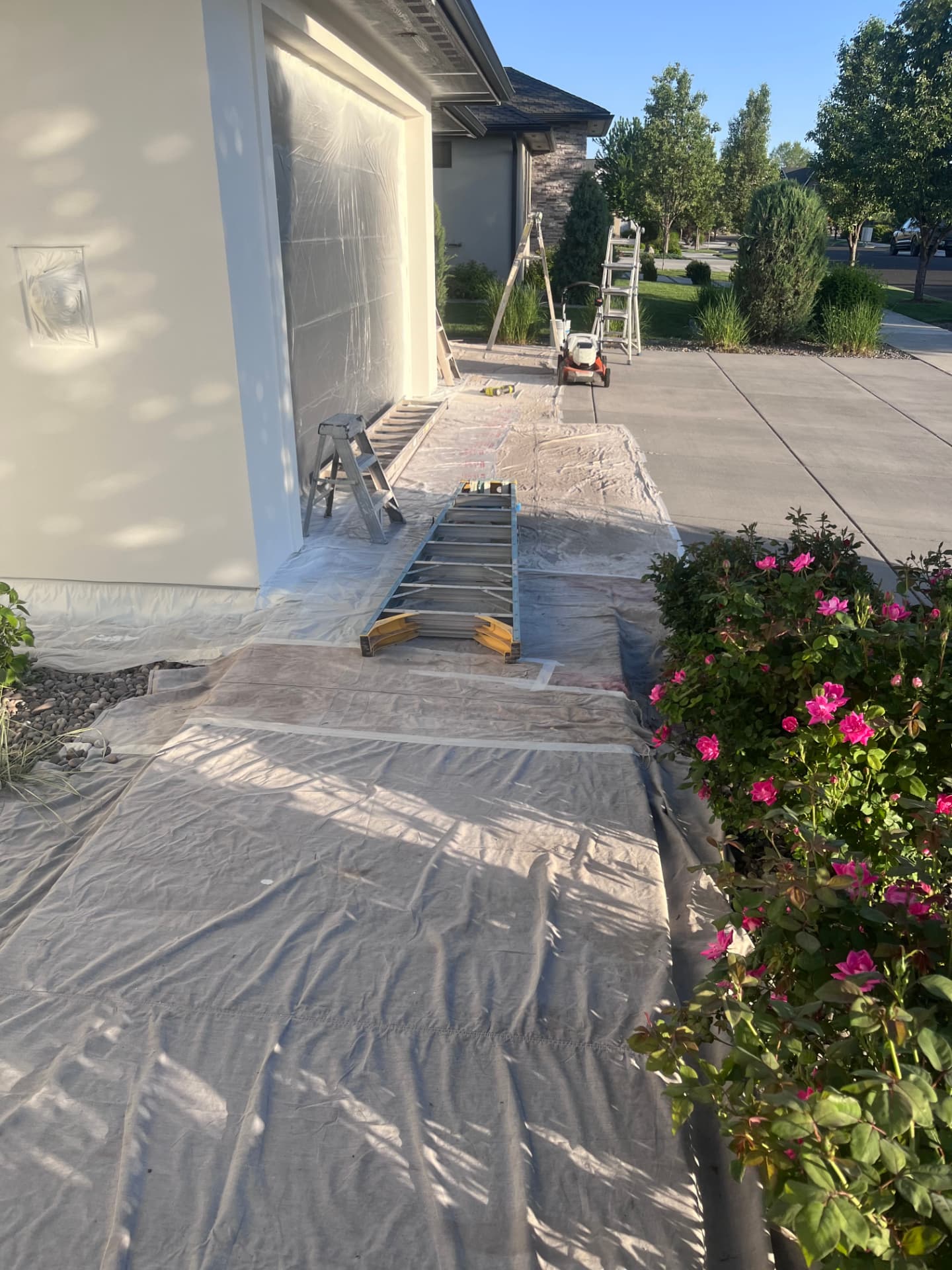 Driveway, garage door, and shrubs covered with drop cloths during preparation
